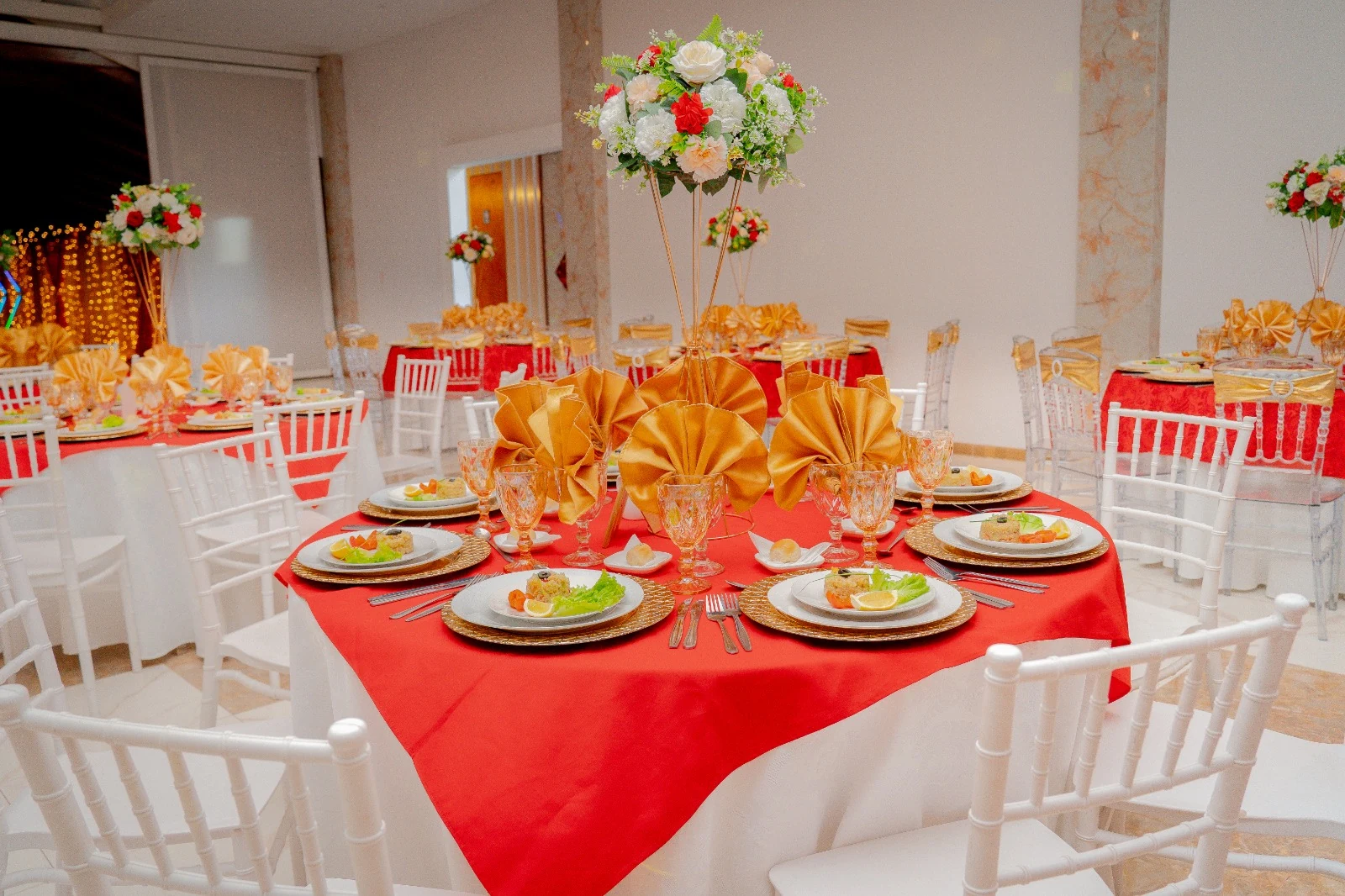 Mesa redonda con mantel rojo, vajilla, cristalería y decoración floral para evento