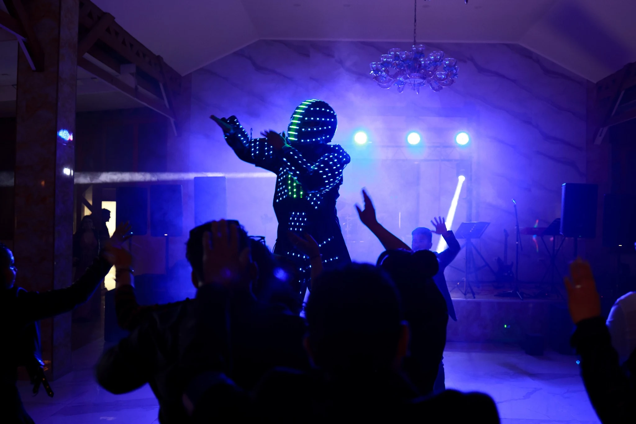 Robot LED azul animando a invitados en una pista de baile con humo y luces