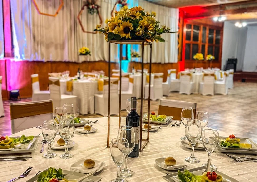 Salón preparado para una licenciatura con mesas, cristalería e iluminación.
